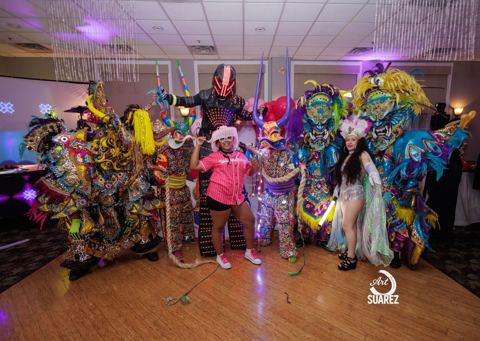ACM performers and community members gather in colorful Carnaval costumes at an indoor celebration